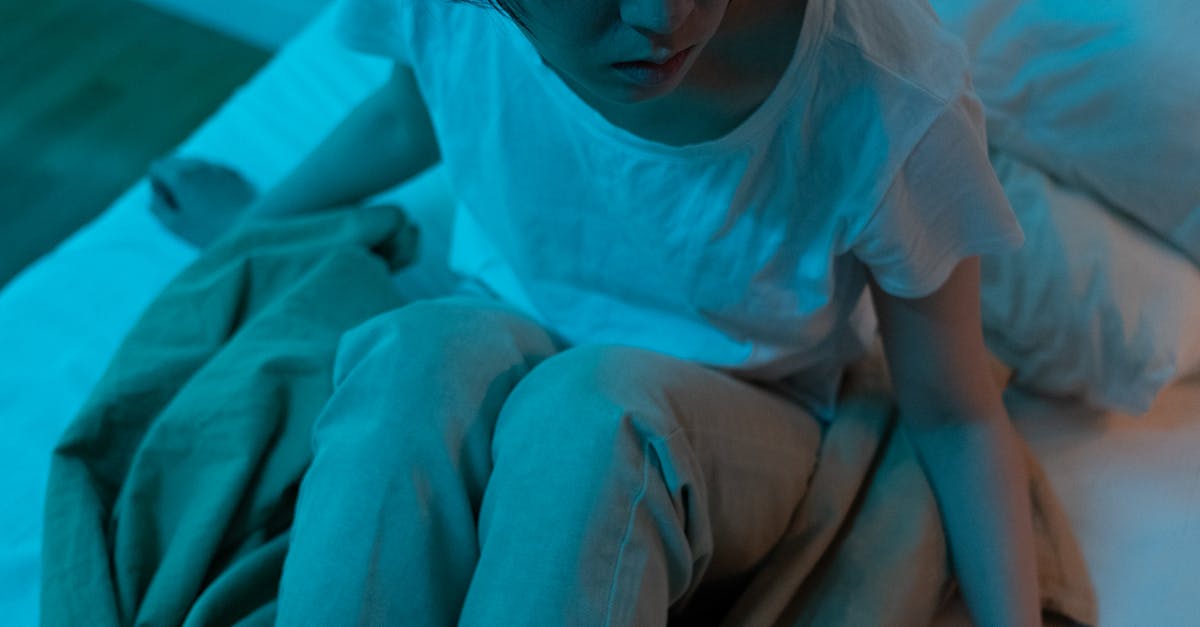 A tired woman sitting on a bed at night looking stressed and restless.